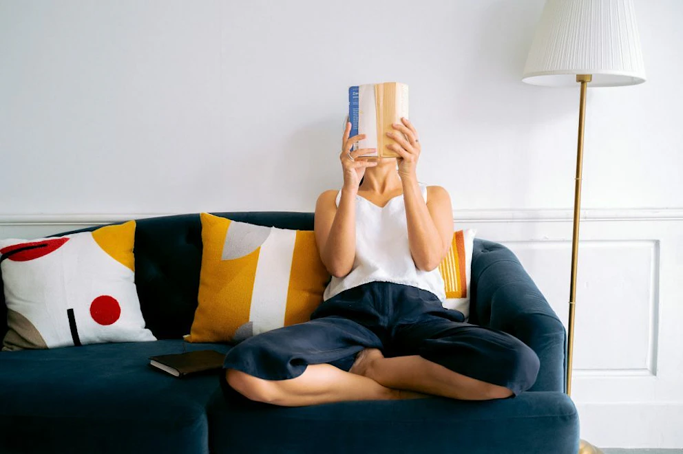 Jeune femme en tailleur sur son canapé lisant un livre