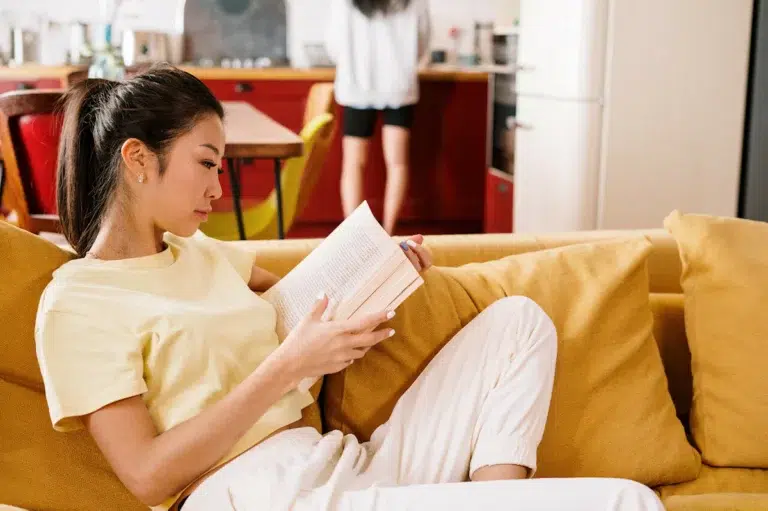 Jeune femme lisant un livre sur son canapé moutarde