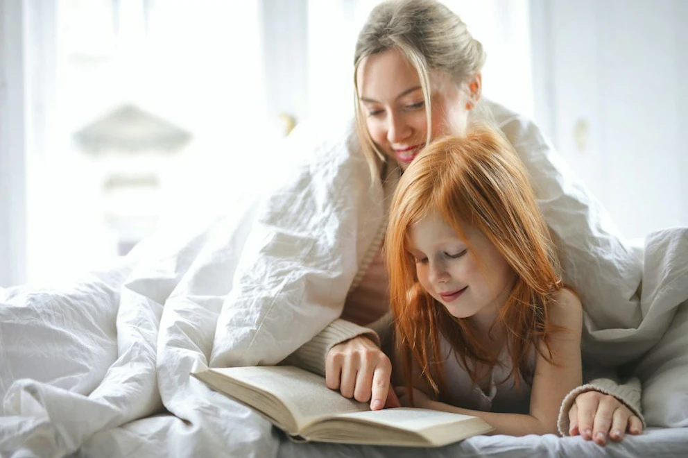Une mère lit un livre à sa petite fille sous la couette