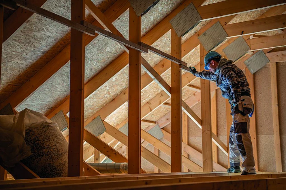 Ouvrier en bleu de travail se tenant sur une poutre dans un grenier en travaux