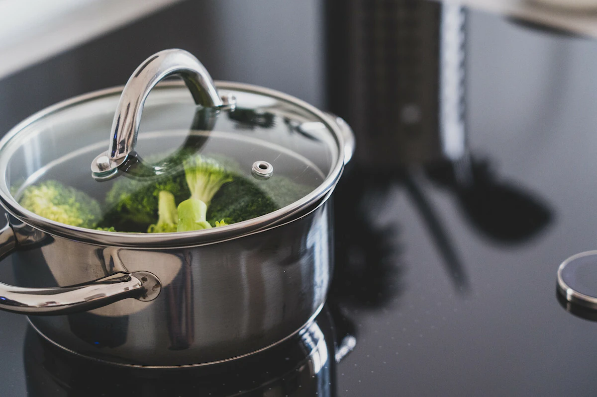 Casserole en inox remplie de brocolis sur une plaque de cuisson
