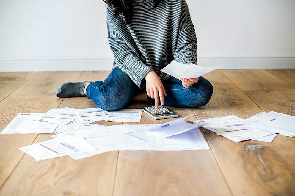 Jeune femme assise au sol parmi des documents éparpillés et tapant sur une calculatrice