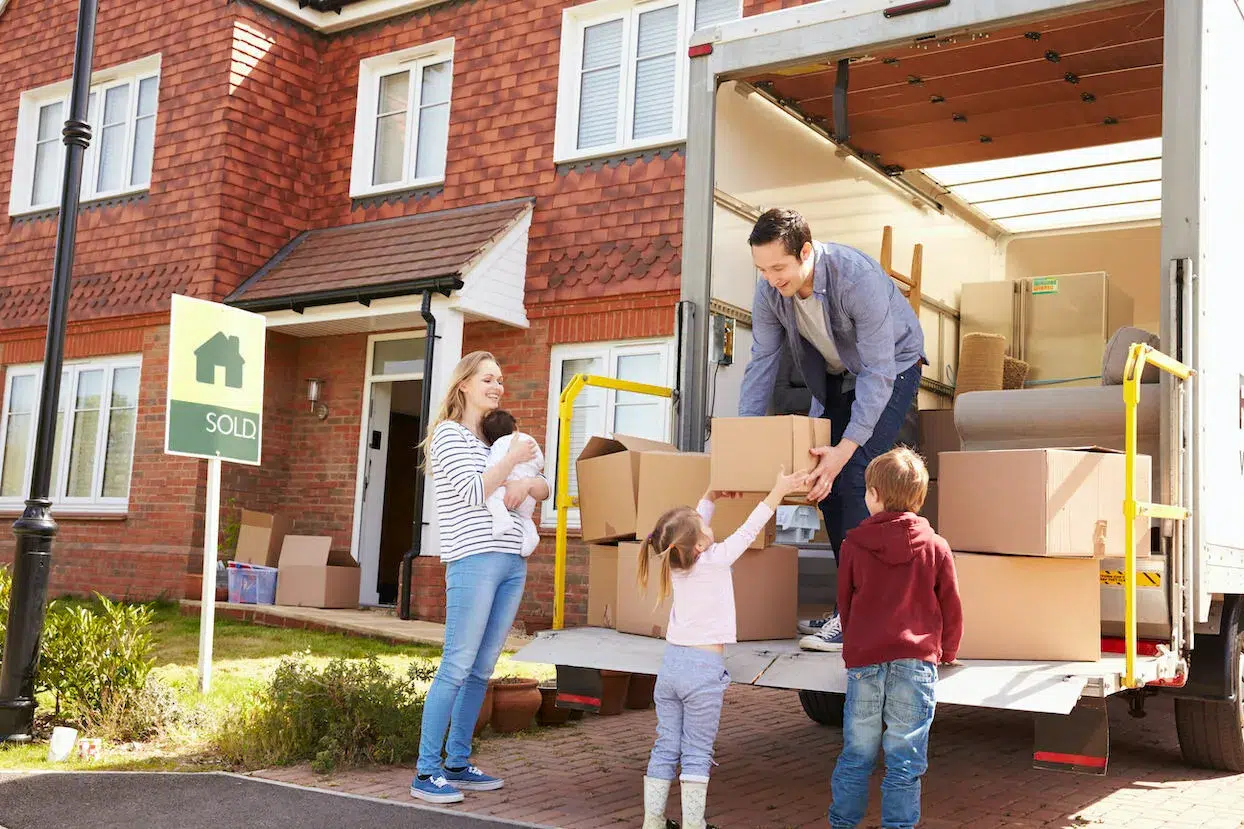 Famille déchargeant un camion de déménagement dans l'allée de leur nouvelle maison, le père passant un petit carton à sa petite fille