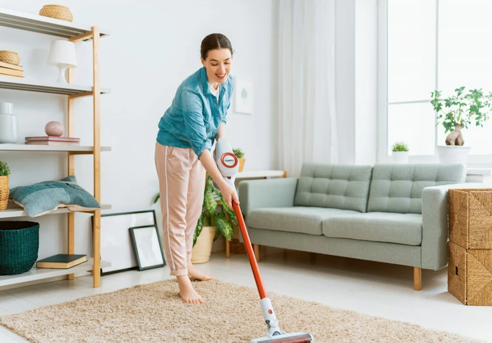 Une jeune femme passant l'aspirateur dans son salon avec le sourire