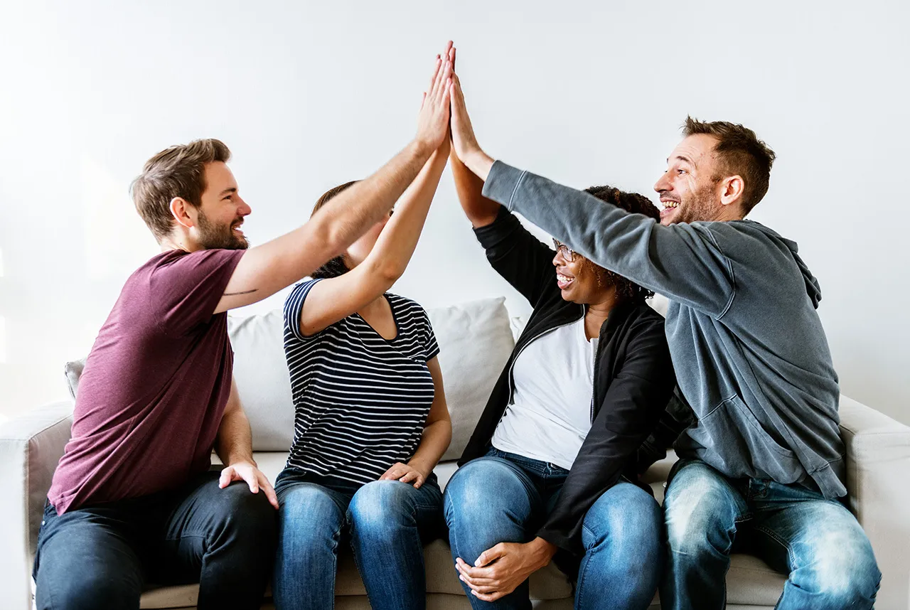 4 jeunes amis assis sur un canapé se tapant dans les mains heureux