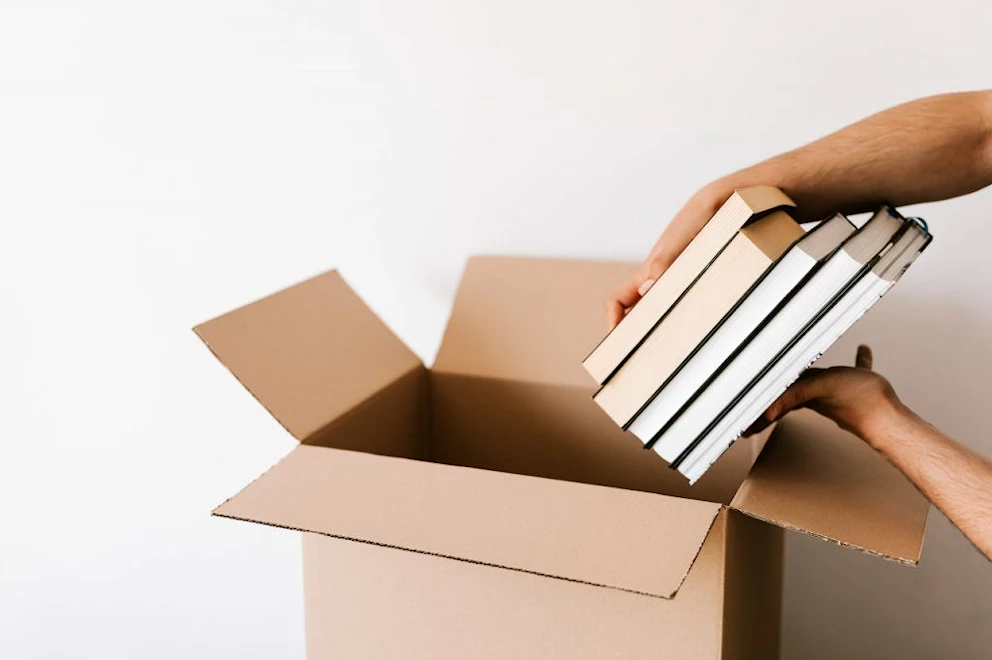 Une personne met une pile de livres dans un carton vide