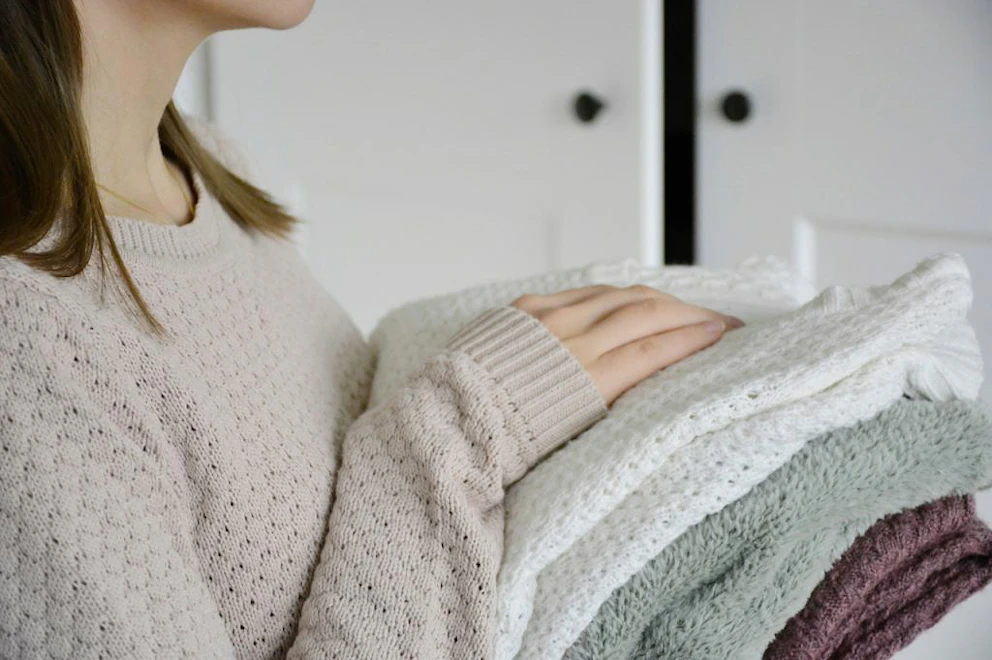 Jeune femme tenant une pile de pull d'hiver pour les ranger dans un placard