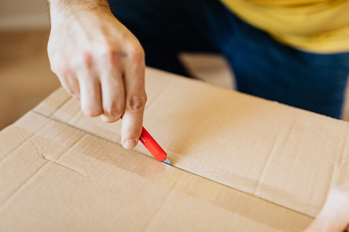 Un homme découpe un carton à l'aide d'un cutter rouge
