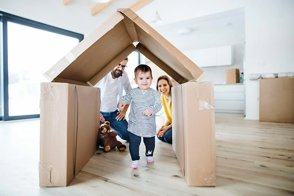 Un enfant passant sous une cabane faite en cartons de déménagement