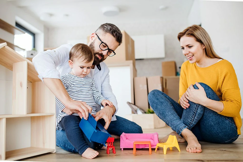 Un homme et une femme jouant avec leur enfant au sol parmi les cartons de déménagement