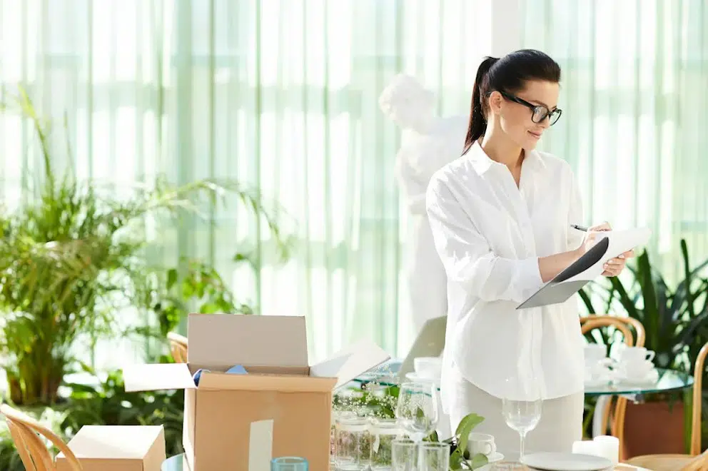 Une femme notant sur un document devant des objets pas encore emballés et mis en carton