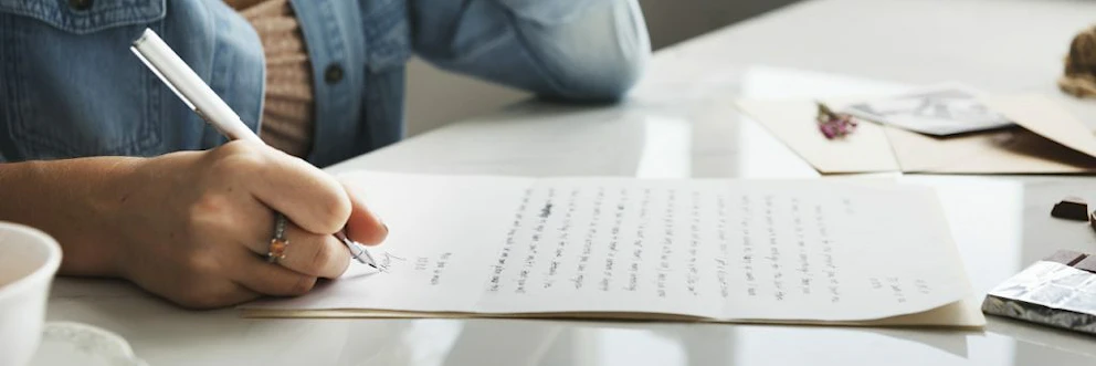 Une femme qui rédige une lettre au stylo sur un bureau