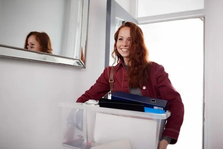 Jeune femme souriante rentrant chez elle une boîte remplie d'affaires dans les mains