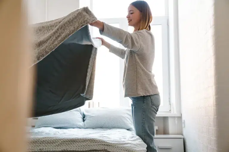 Une jeune femme est en train de faire son lit en remettant la couverture correctement