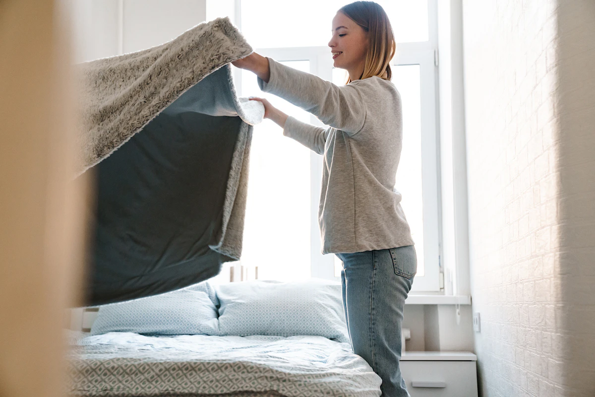 Une jeune femme est en train de faire son lit en remettant la couverture correctement