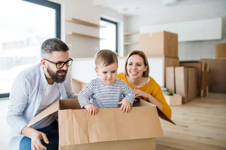 Un bébé dans un carton de déménagement entouré de ses parents souriants