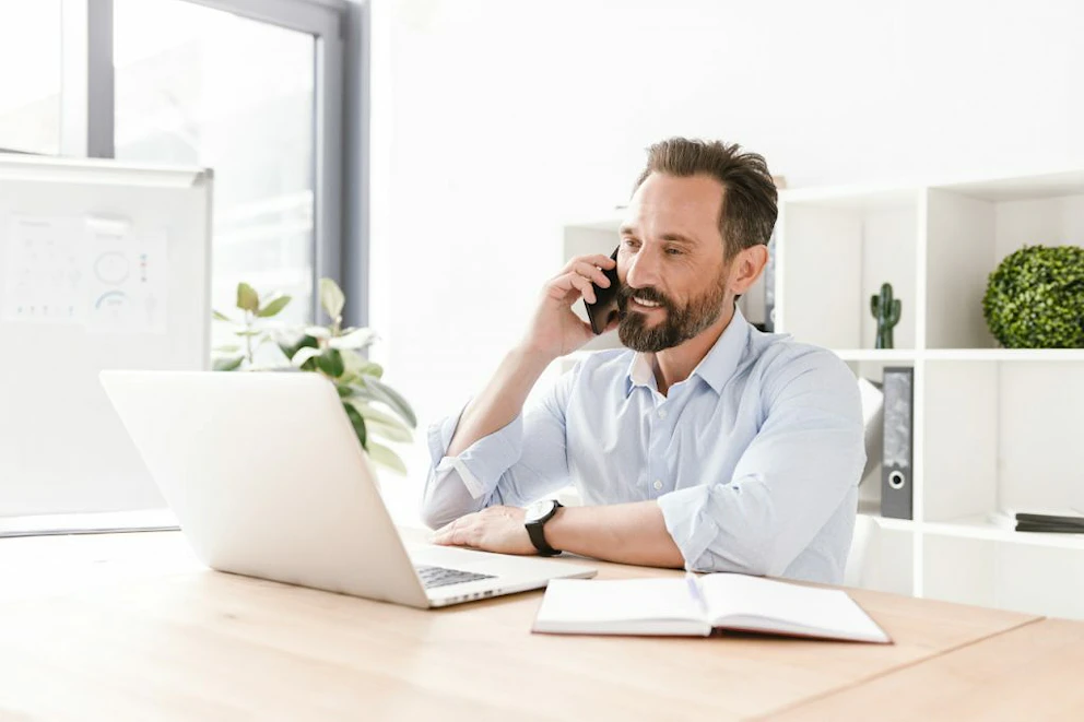 Homme barbu au téléphone devant son ordinateur portable
