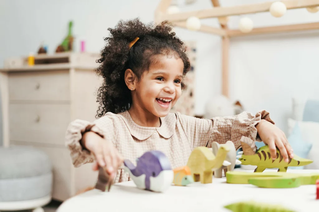Petite fille joyeuse jouant avec des dinosaures en bois sur une petite table dans sa chambre