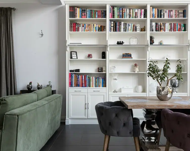 Espace salle à manger avec une table en bois, des fauteuils noir et une bibliothèque blanche
