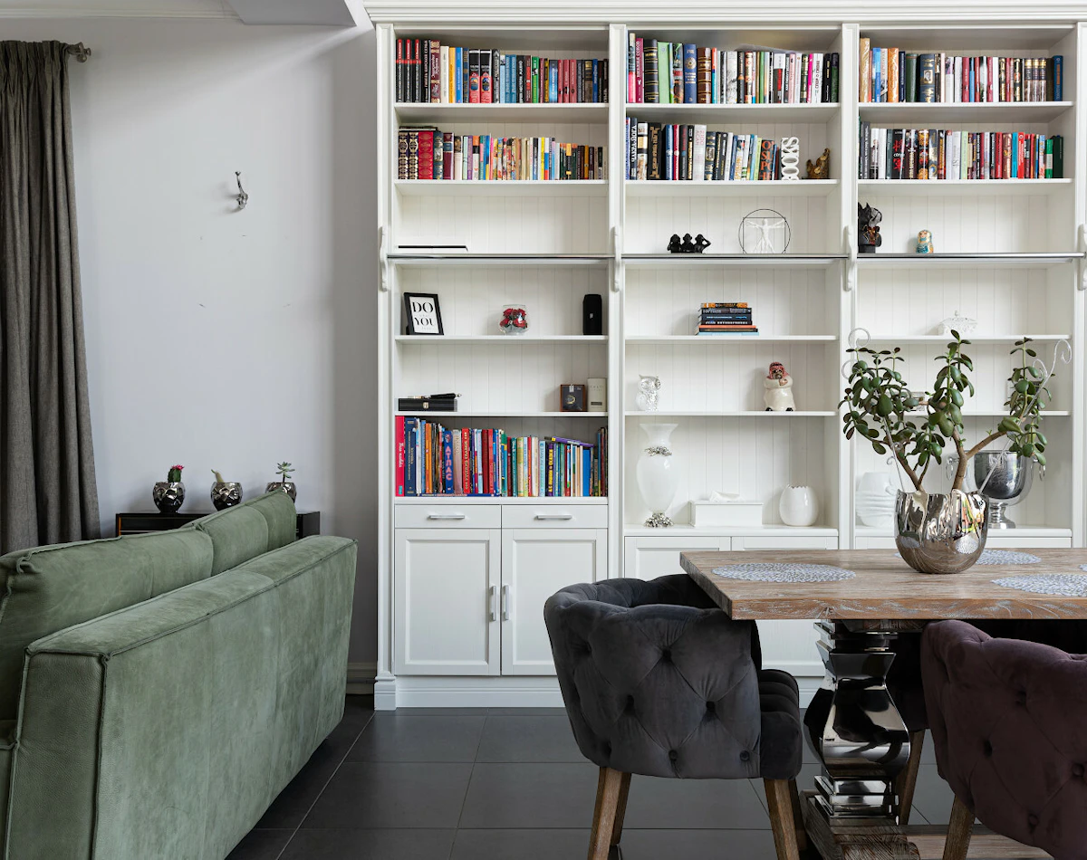 Espace salle à manger avec une table en bois, des fauteuils noir et une bibliothèque blanche