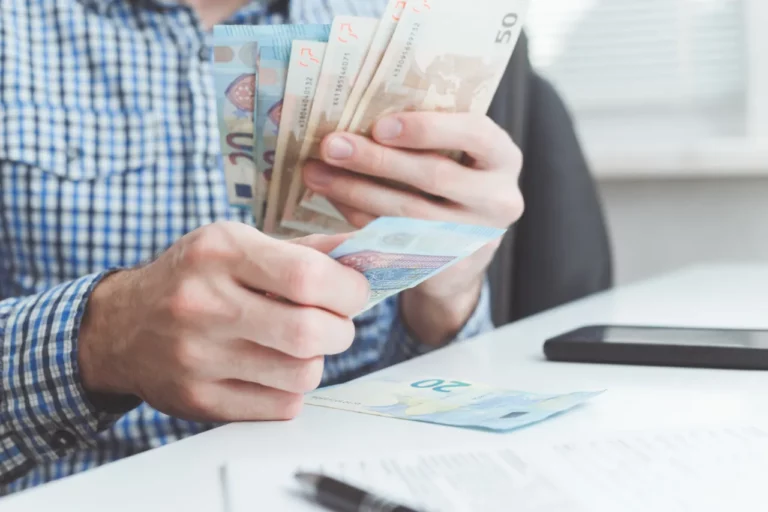 Homme en chemise à carreaux compte des billets de 50 et 20 euros sur son bureau