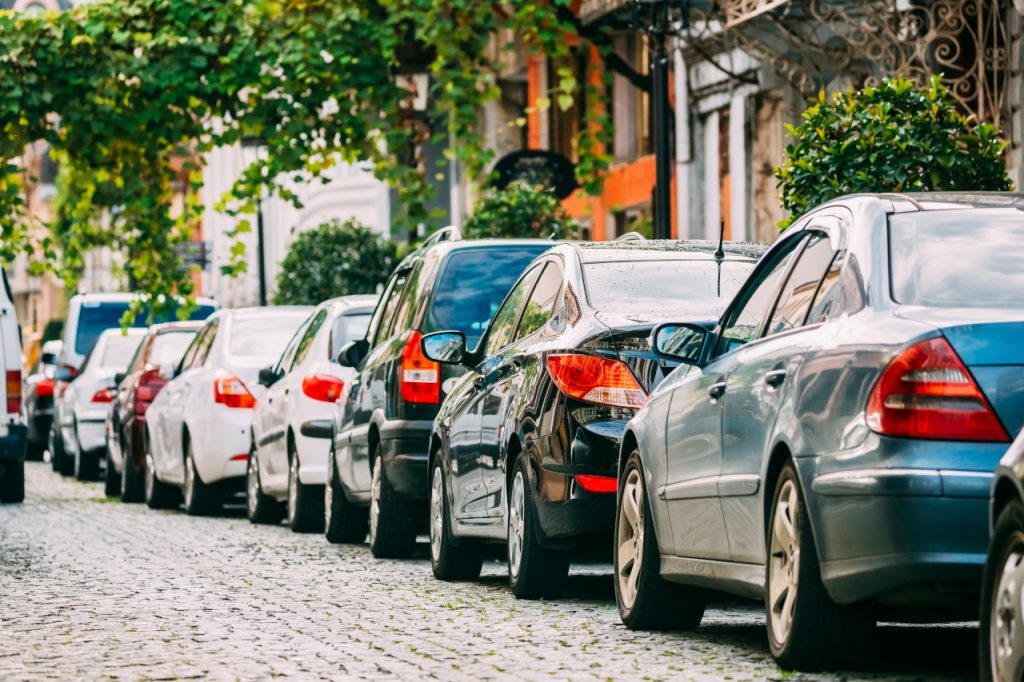 File de voitures garées sur le côté d'une voie pavée devant des habitations