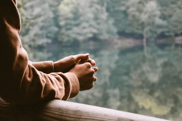 A person leaning on a railing facing a lake
