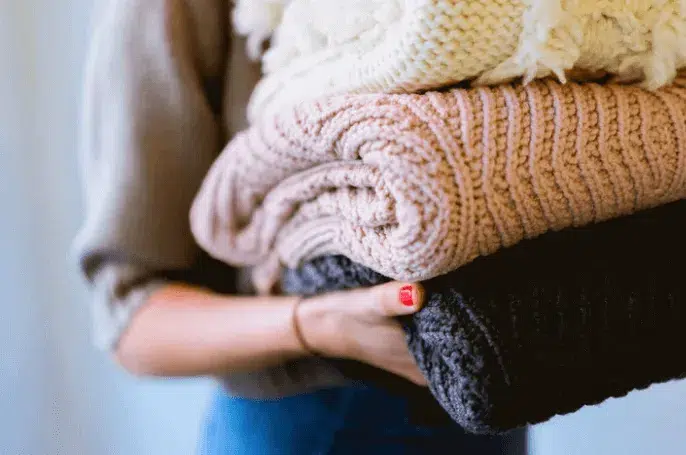 Woman carrying a pile of woollen jumpers