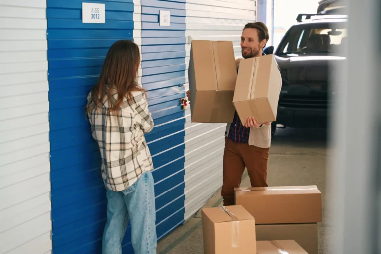 Happy couple are puting together cardboard boxes with things into self storage container of warehouse