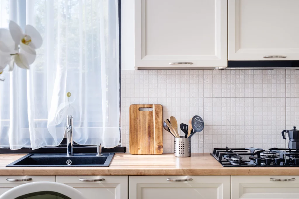 Zoom sur le plan de travail d'une cuisine blanche et bois, l'évier les placards et la plaque de cuisson au gaz