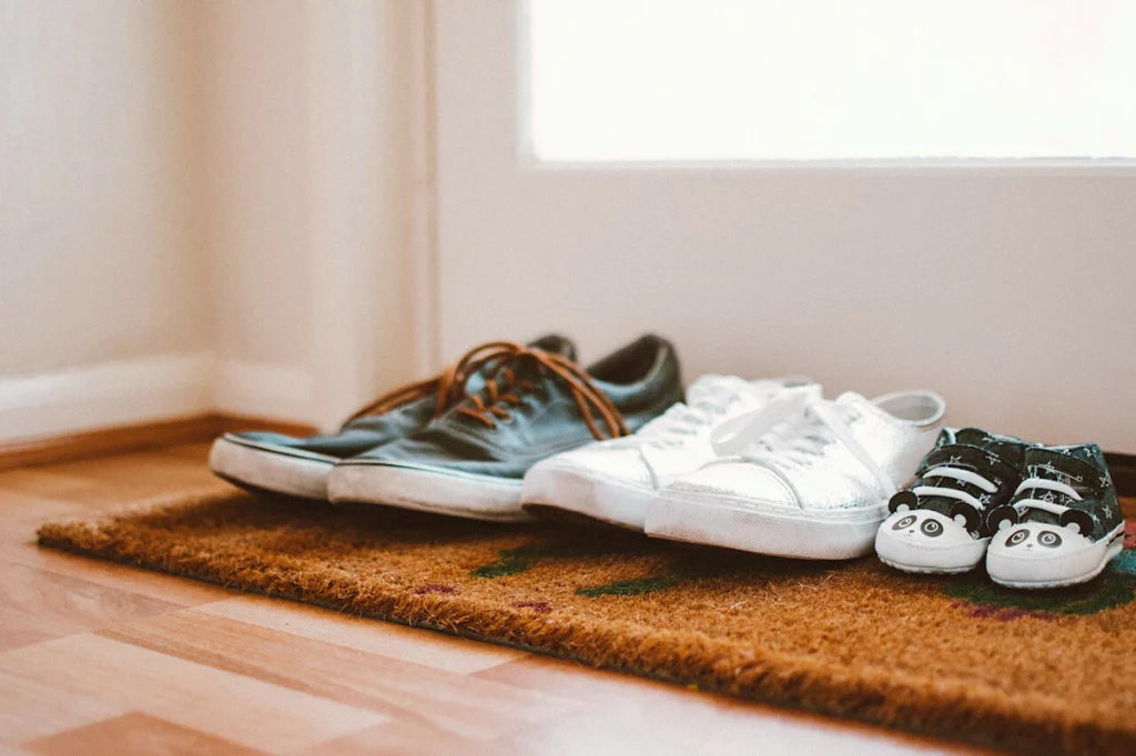3 paires de chaussures alignées sur le paillasson à l'entrée de la maison