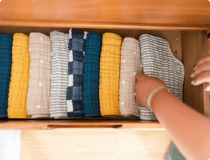 A young woman picking up a baby's nappy from a pile in a drawer.