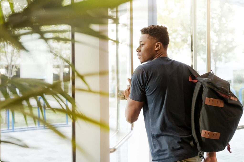 A student carrying a backpack exits a building.