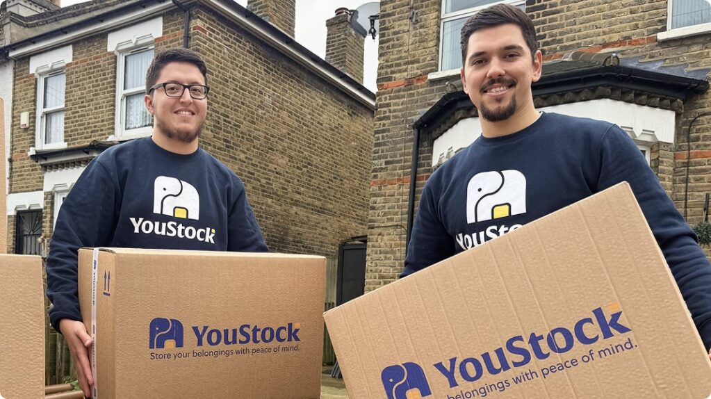 Two YouStock movers carrying a YouStock branded cardboard box - Store your belongings with peace of mind.