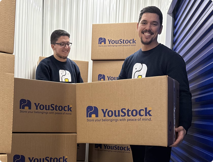 Two YouStock movers carrying a YouStock branded cardboard box - Store your belongings with peace of mind.