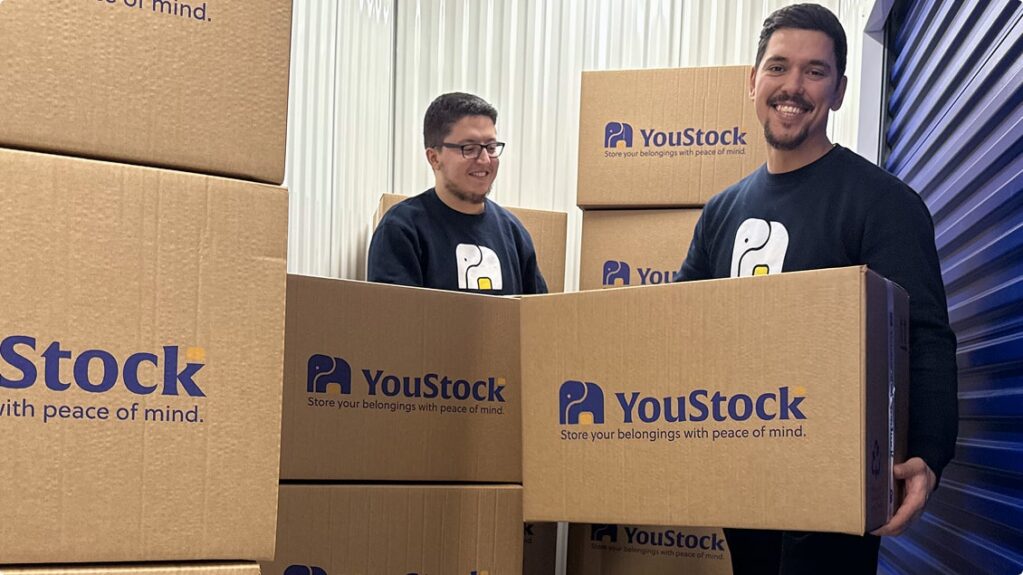 Two YouStock movers each carry a YouStock branded cardboard box - Store your belongings with peace of mind.