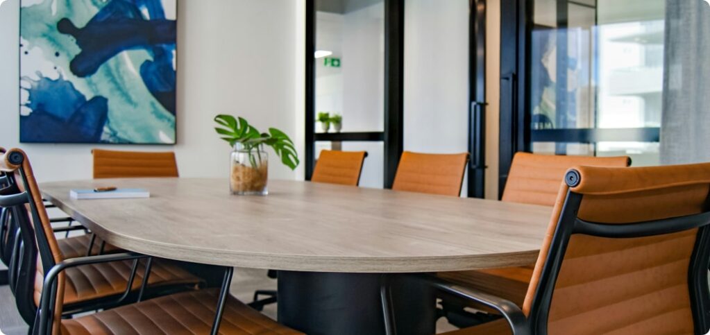 A meeting room filled with an oval wooden table with office chairs