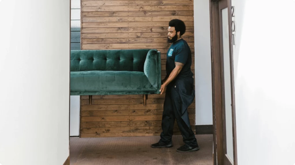 A removal man carries a sofa.