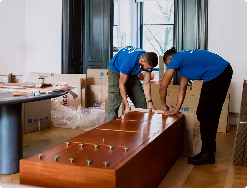 deux déménageurs YouStock emballent et protègent un grand meuble pour le déménager