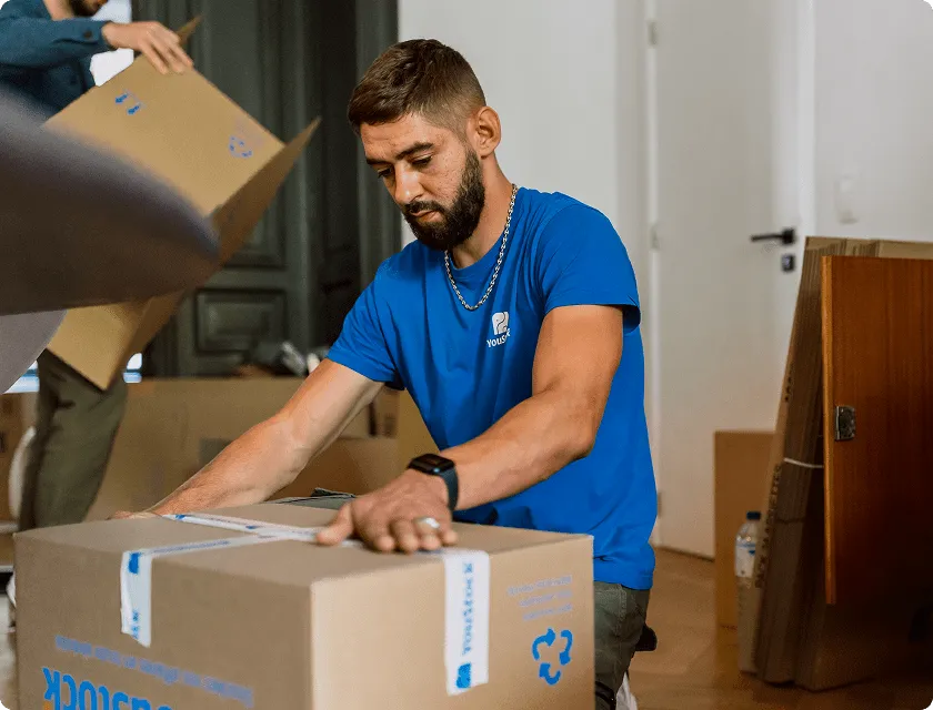A YouStock mover tapes a moving/storage box to the floor.