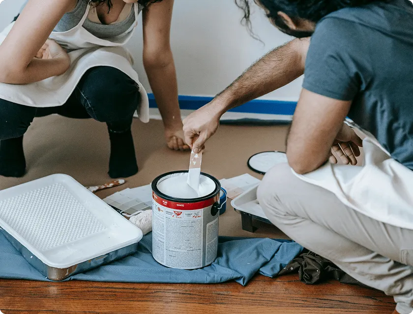 A man mixes a pot of paint on the floor.