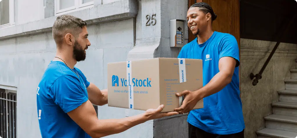 Two YouStock removal men pass each other a storage box.