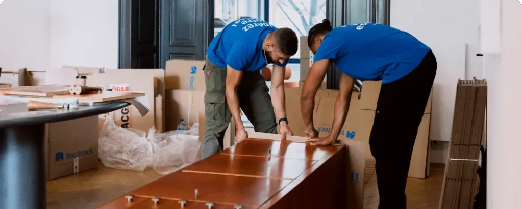 Two YouStock removal men pack and protect a piece of furniture for storage.