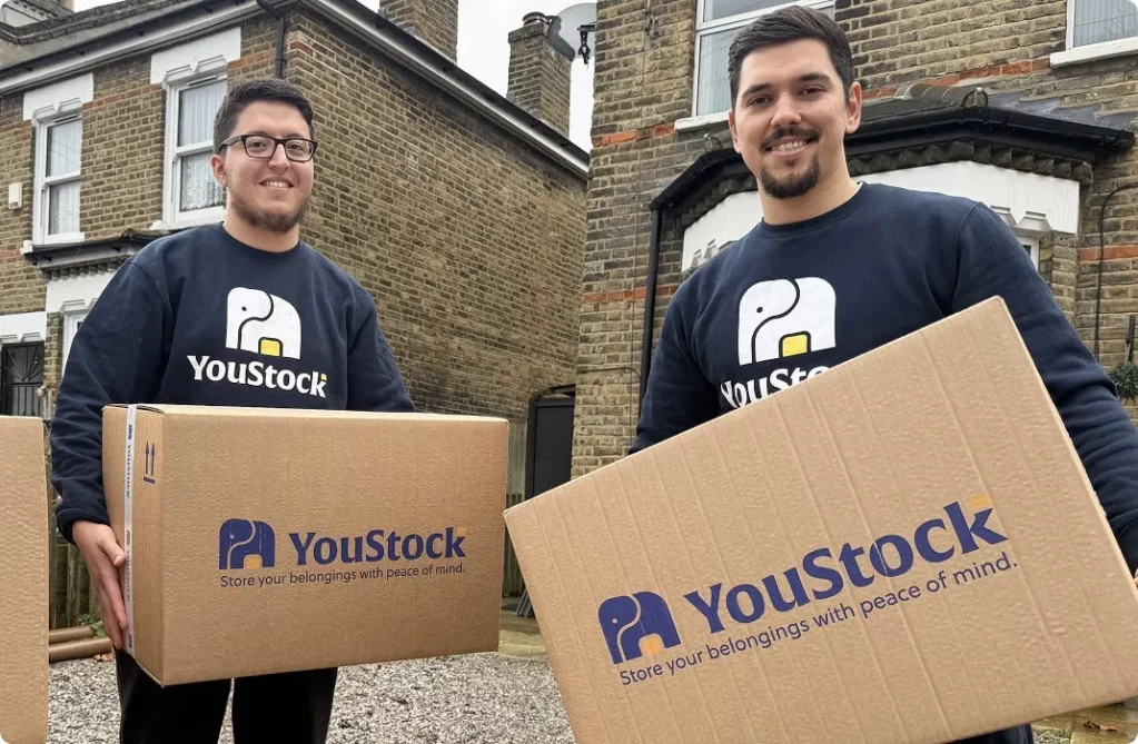Two YouStock movers each carry a YouStock branded cardboard box - Store your belongings with peace of mind.