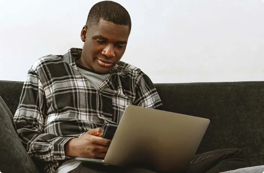 Jeune homme assis sur un canapé avec son ordinateur portable sur les genoux