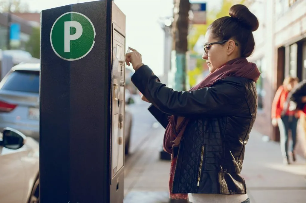 Jeune femme devant un parcmètre sur le trottoir d'une rue