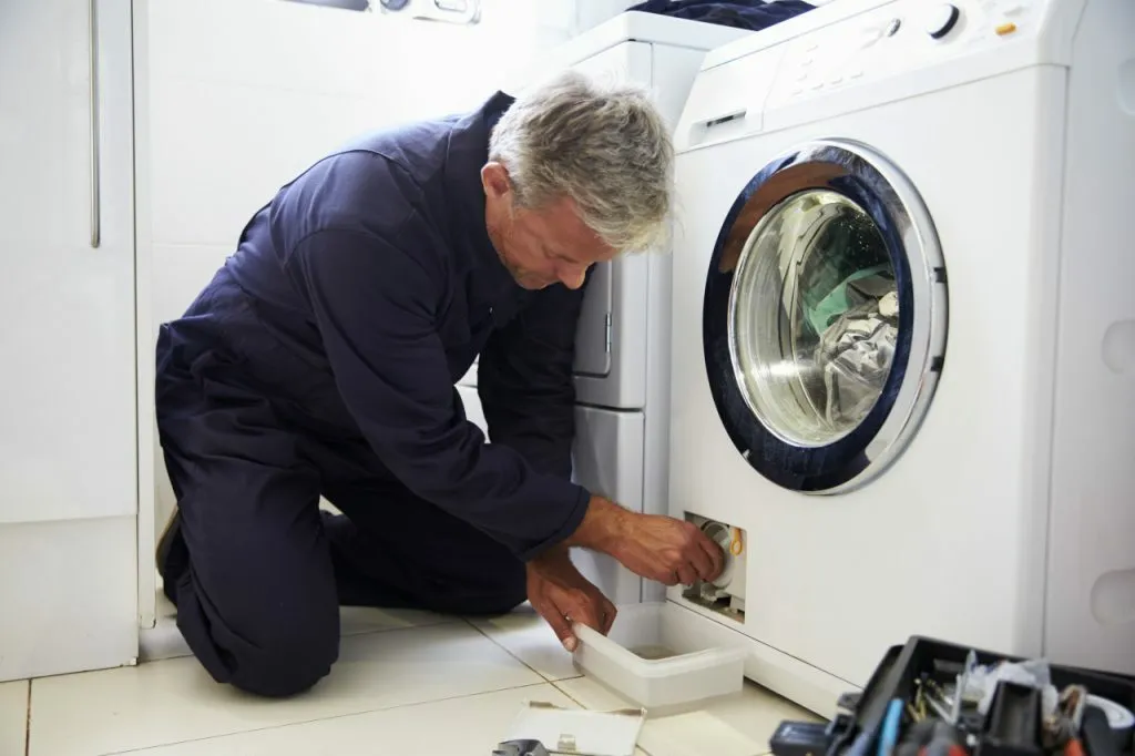 Homme en bleu de travail à genoux en train de vidanger un lave-linge
