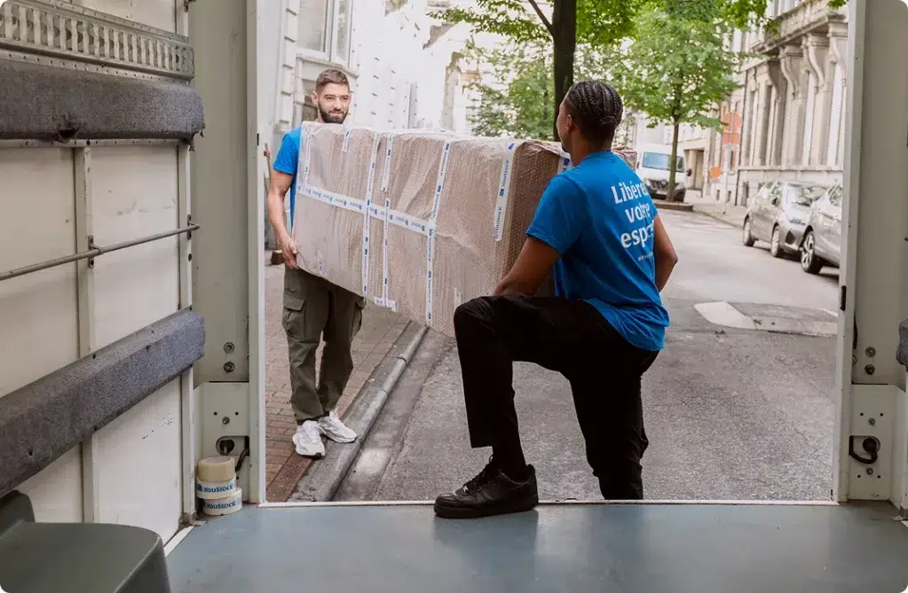 Deux professionnels YouStock portent un meuble emballé et protégé à l'arrière d'un camion de déménagement