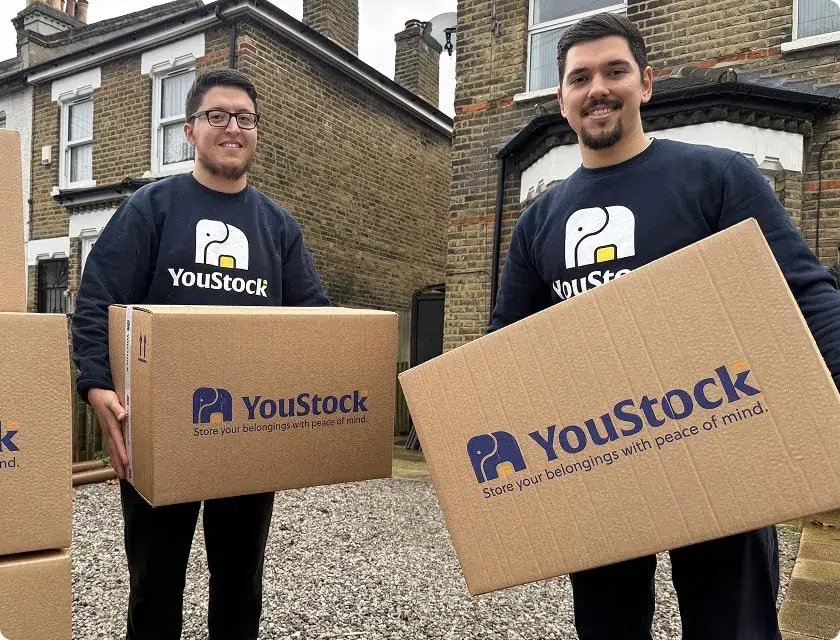 Two YouStock movers, each holding a moving box in their hands