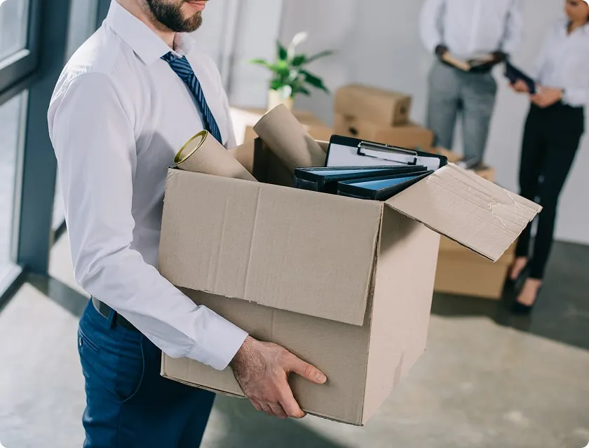 Man in shirt and tie carries moving box filled with office supplies